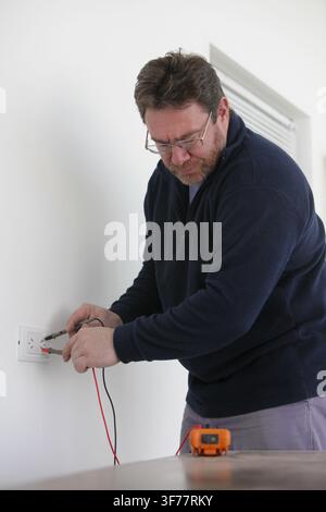 Electrician testing an electrical outlet with a digital multimeter during home electrical repair and maintenance. Modern electrical work, wiring inspe Stock Photo
