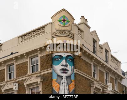 A vibrant portrait mural adorns a historic building on Portobello Road, Notting Hill, showcasing modern street art in a classic London spot. Stock Photo