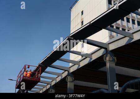Workers on a lift install structural steel for the new Elizabeth line entrance canopy at Ealing Broadway station. Stock Photo