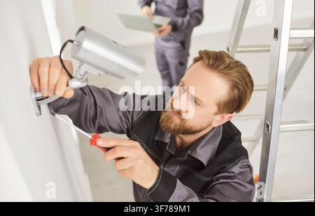 Portrait of young technician man installing surveillance CCTV camera on wall indoors Stock Photo