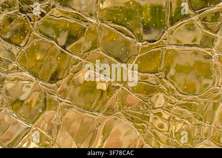 Close-up of golden textured glass with irregular reflections, abstract luxury background with warm translucent surface. Stock Photo