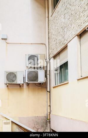 Building facade with air conditioners, drainage pipes, and windows with closed shutters. Stock Photo