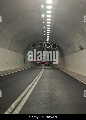 a serene first-person view of a car driving through an industrial tunnel, showcasing concrete and metal structures with ventilation fans and bright li Stock Photo
