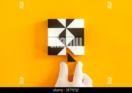 Software patching and micro vulnerability concept. Hand in white glove fixing a small geometric piece in a digital puzzle system on yellow background Stock Photo