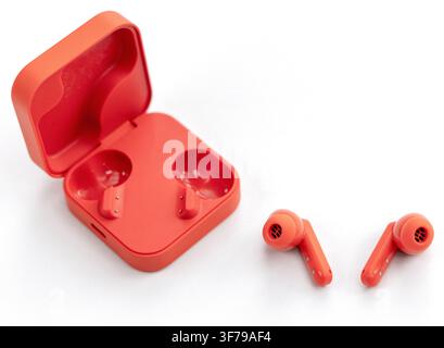 Bright orange wireless earbuds rest beside their open charging case Stock Photo