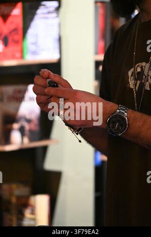 A close-up photograph capturing a DJ's hands, adorned with silver rings and a watch, meticulously adjusting the delicate stylus (needle) on a vinyl record player cartridge. The turntable is playing a record, and blurred vinyl shelves are in the background. Stock Photo