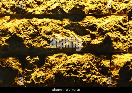 A horizontal photograph capturing a close-up of a textured ceramic wall with a rough, uneven surface, illuminated by warm yellow lighting. Stock Photo