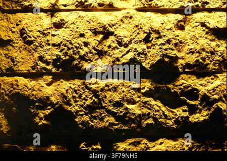 A horizontal photograph capturing a close-up of a textured ceramic wall with a rough, uneven surface, illuminated by warm yellow lighting. Stock Photo