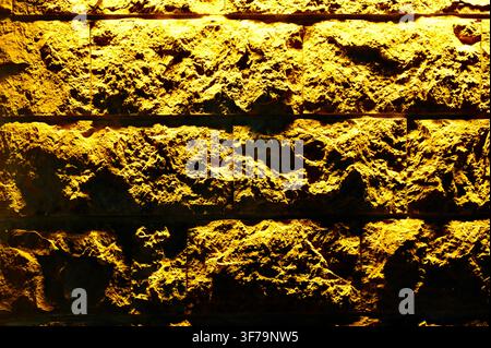 A horizontal photograph capturing a close-up of a textured ceramic wall with a rough, uneven surface, illuminated by warm yellow lighting. Stock Photo