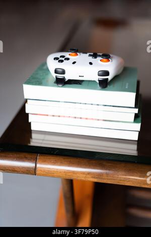 White gaming controller resting on a stack of books atop a wooden table with glass top — modern Stock Photo
