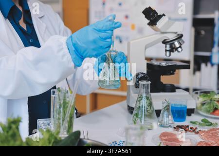 Scientists in lab coats work with plants in a modern lab, focusing on research and experimentation under bright, sterile conditions. Stock Photo