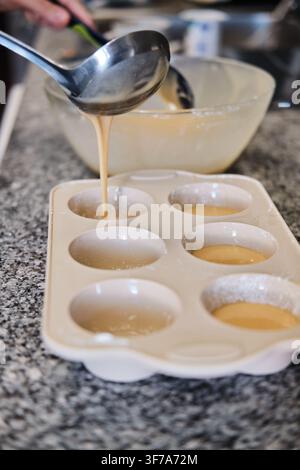 Person pouring cake batter using a ladle into a silicone muffin pan on a kitchen counter Stock Photo