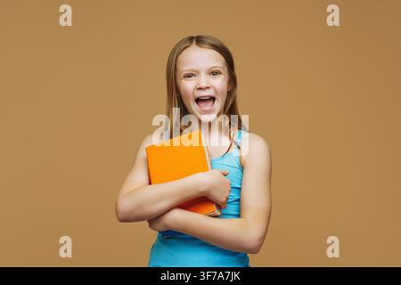 A happy schoolgirl with a books stands on an isolated background. Back to school and joy of learning concept. Stock Photo