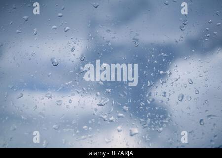 Raindrops cling to the glass, creating a mosaic of shapes and sizes against an overcast sky, where distant clouds drift slowly across the horizon in m Stock Photo