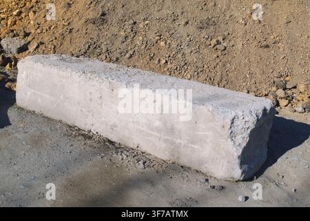 A rectangular concrete block is prominently featured on a sandy surface with visible dirt and rocks scattered around. The block appears freshly laid, Stock Photo