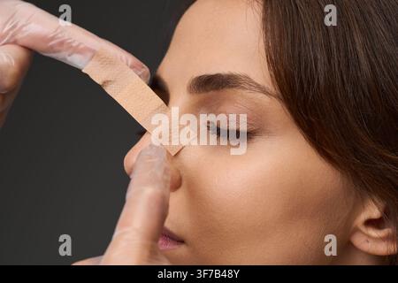 Doctor examining nasal taping on a young woman following a rhinoplasty and septoplasty operation. Surgeon adjusting adhesive tape on the nose of a fem Stock Photo