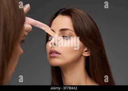 Doctor examining nasal taping on a young woman following a rhinoplasty and septoplasty operation. Surgeon adjusting adhesive tape on the nose of a fem Stock Photo