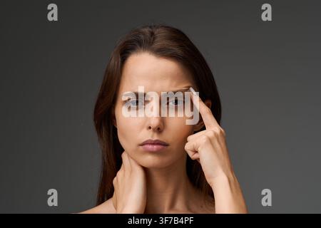 Stressed young woman suffering from a severe migraine and neck ache. Female patient holding her neck and touching her head, demonstrating referred pai Stock Photo
