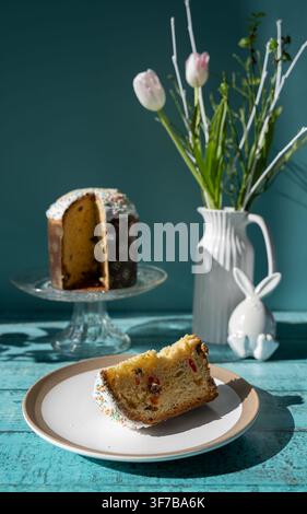 Traditional Eastern European Paska also known as Pasca served with a slice on a plate alongside fresh tulips and a decorative Easter bunny on a blue w Stock Photo