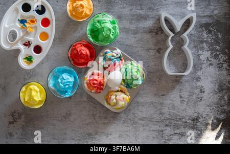 Overhead Easter craft composition featuring colorful painted eggs a watercolor palette and a white bunny decoration arranged on a textured gray backgr Stock Photo