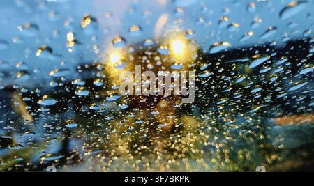 Raindrops on a car windshield with blurred yellow lights in the background Stock Photo