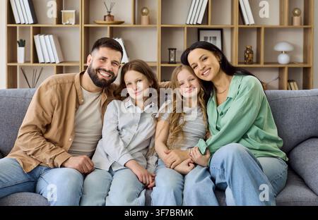 Happy parents with two daughters sitting on sofa at home, smiling portrait Stock Photo