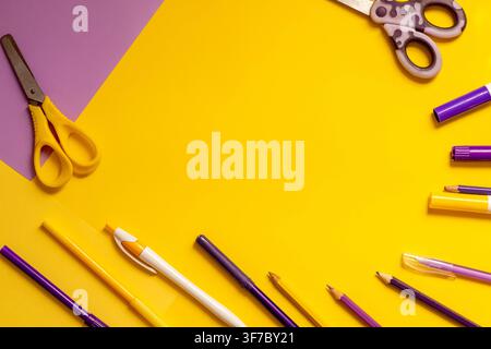 Students prepare for back to school with colors and tools on a table. Scissors, pens, markers, and paper are spread across the yellow and purple surfa Stock Photo