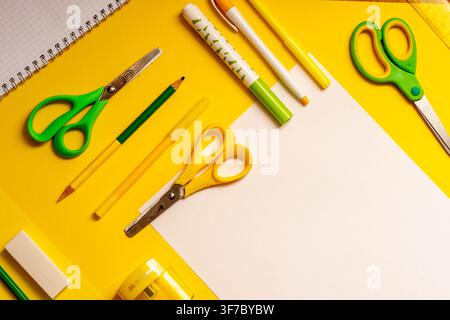 Supplies are placed on a bright yellow table. There are scissors, paper, pens, and markers ready for school activities. Items are arranged neatly with Stock Photo
