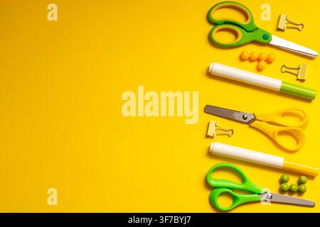 A variety of school tools is arranged on a yellow background. There are scissors, markers, and paper clips. The items are organized in a line. All too Stock Photo