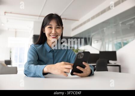 Happy Asian woman using smartphone in coworking office Stock Photo