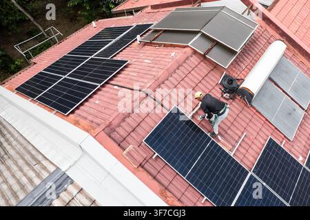 Aerial view of workers installing solar photovoltaic or PV panels onto red rooftop of residential house in Malaysia Stock Photo