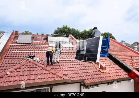 Aerial view of workers transporting solar photovoltaic or PV panels with crane onto red rooftop of residential house to install in Malaysia Stock Photo