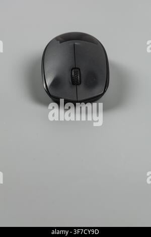 A wireless computer mouse sits on a plain surface in an office setting. It is ready for work. Stock Photo