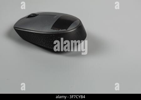A black wireless computer mouse sits on a clean office desk. This device aids in daily tasks. Stock Photo