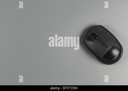 A wireless mouse rests on a gray desk while someone works at a computer in an office setting. Stock Photo