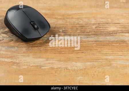 A black computer mouse rests on a wooden desk in a business setting during the day. Stock Photo