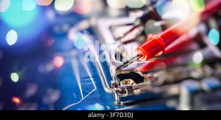 Abstract tech background. Macro view of a red multimeter probe on a computer motherboard CPU socket with colorful glowing bokeh lights. Stock Photo
