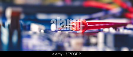 Hardware diagnostics. Red test lead of a digital multimeter on a blurred computer motherboard background. Stock Photo