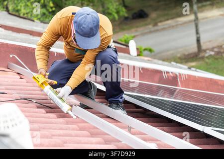 Worker installing mounting brackets onto red residential roof for solar photovoltaic or PV panels in Malaysia Stock Photo