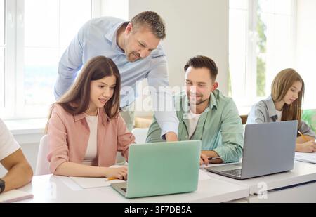 Teacher guiding college students on laptop during interactive classroom lesson Stock Photo
