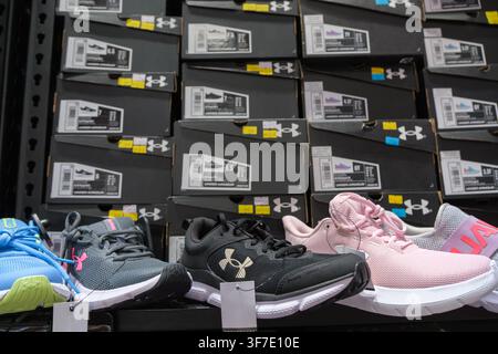 A store display shows several Under Armour shoes in different colors arranged on a wall, with their packaging Stock Photo