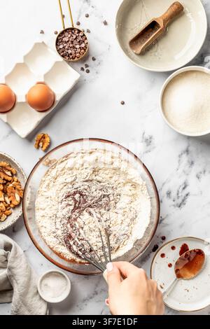 Process of making chocolate brownie. Female hands mix flour with the dough in glass bowl, top view. Home baking culinary concept, recipe Stock Photo