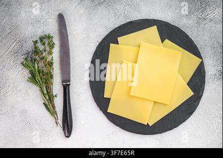 Yellow sliced cheese arranged on black slate platter with herbs on light stone background, rustic dairy food with copy space. Stock Photo