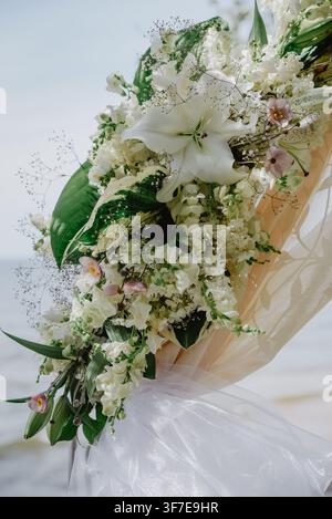 Elegant close-up of a white floral wedding arch featuring lilies, hydrangeas, delicate baby's breath, greenery and flowing fabric, creating a romantic Stock Photo