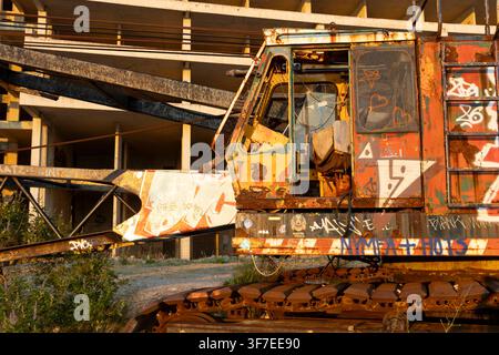 This image captures an abandoned industrial site featuring rusted metal structures, graffiti-covered walls, and overgrown vegetation, set against the Stock Photo