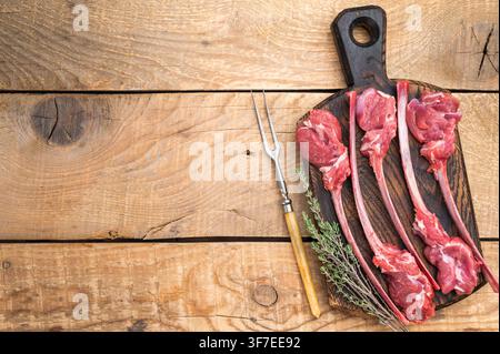 Premium raw lamb ribs and cutlets on rustic wood board with herbs light background top view food concept Stock Photo