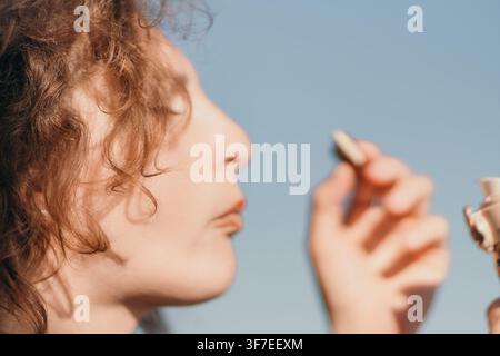 Woman, bubbles, face, profile view of a young woman blowing soap bubbles against a clear blue sky outdoors with natural sunlight Stock Photo