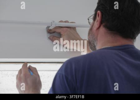 Man measuring and marking the wall above a window with pencil to drill holes for installing a curtain rod and brackets. Stock Photo