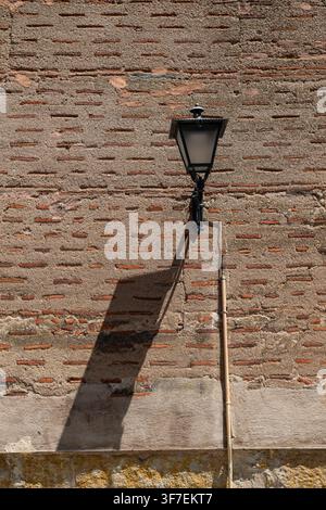 A classic black lantern mounted on a historic brick wall and its distinct shadow cast on the wall. Stock Photo
