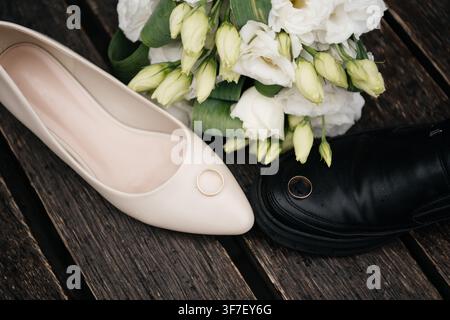 Bride and groom wedding shoes with two golden rings and a white bouquet on a rustic wooden surface Stock Photo